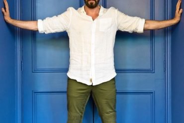 Richard Armitage against blue door with his arms stretched